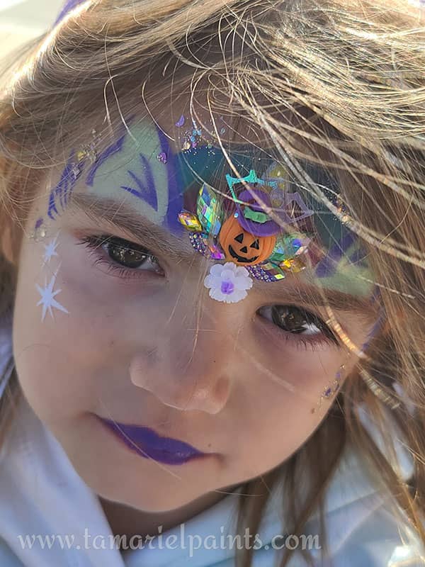 A girl with colorful cat and pumpkin themed airbrush face paint