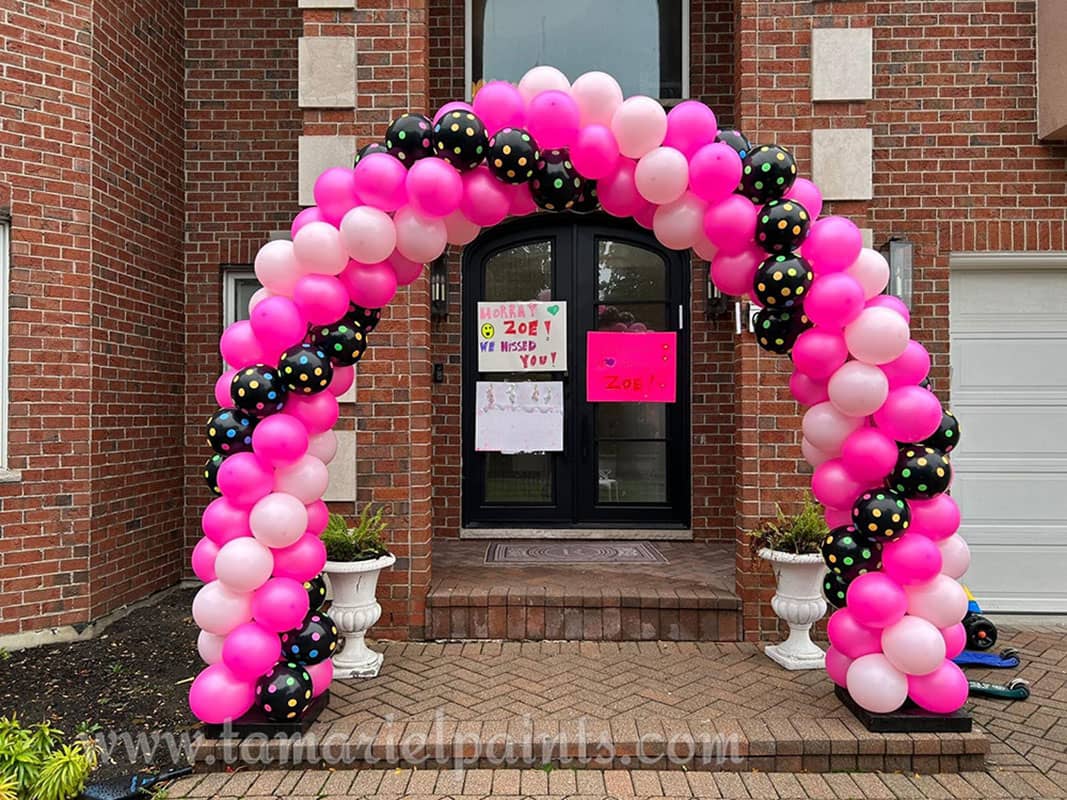 An arch of twisting dark pink light pink and black balloons with polkadots in front of a building entrance