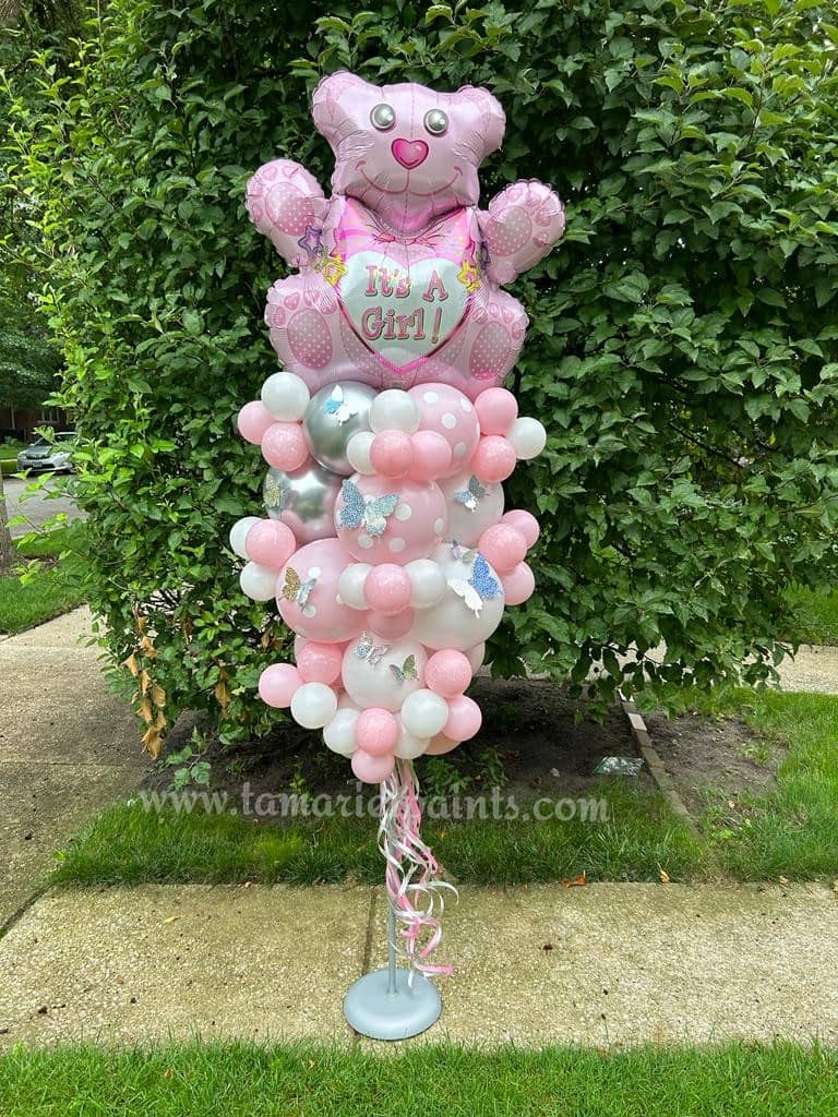 A creative balloon display of pink and white balloons with a teddy bear balloon with It's a Girl text on it