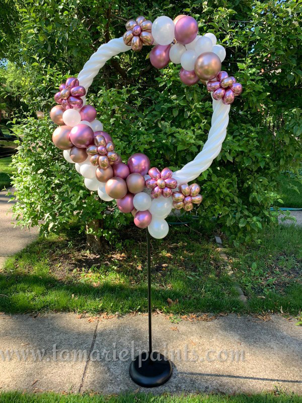 A photo of an artistic, circular, standing balloon display white and pink pearlescent balloons