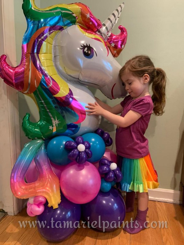 A photo of a child hugging a colorful unicorn balloon display