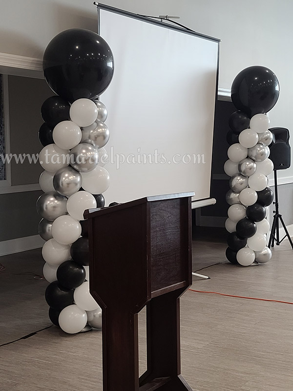 A photo of 2 columns of black, white and silver balloons flanking a projection screen at an event