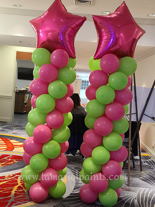 A photo of 2 columns of pick and green balloons with pink star balloons at the top