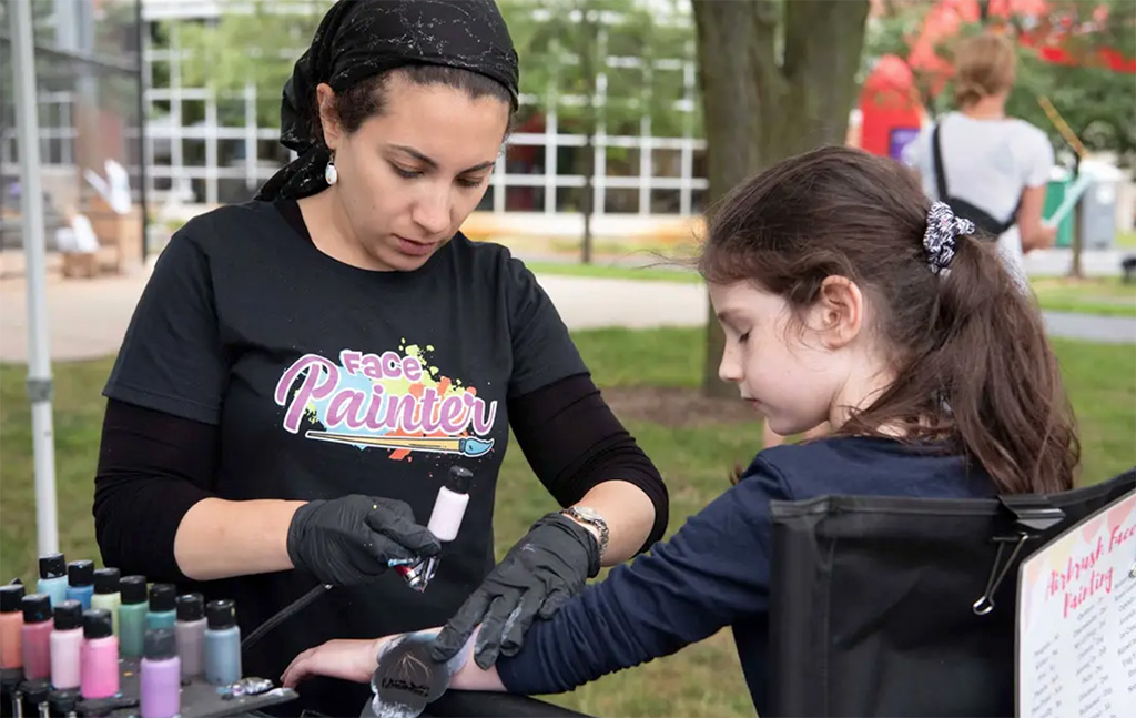 A photo of Tamar airbrushing a design onto a child's arm