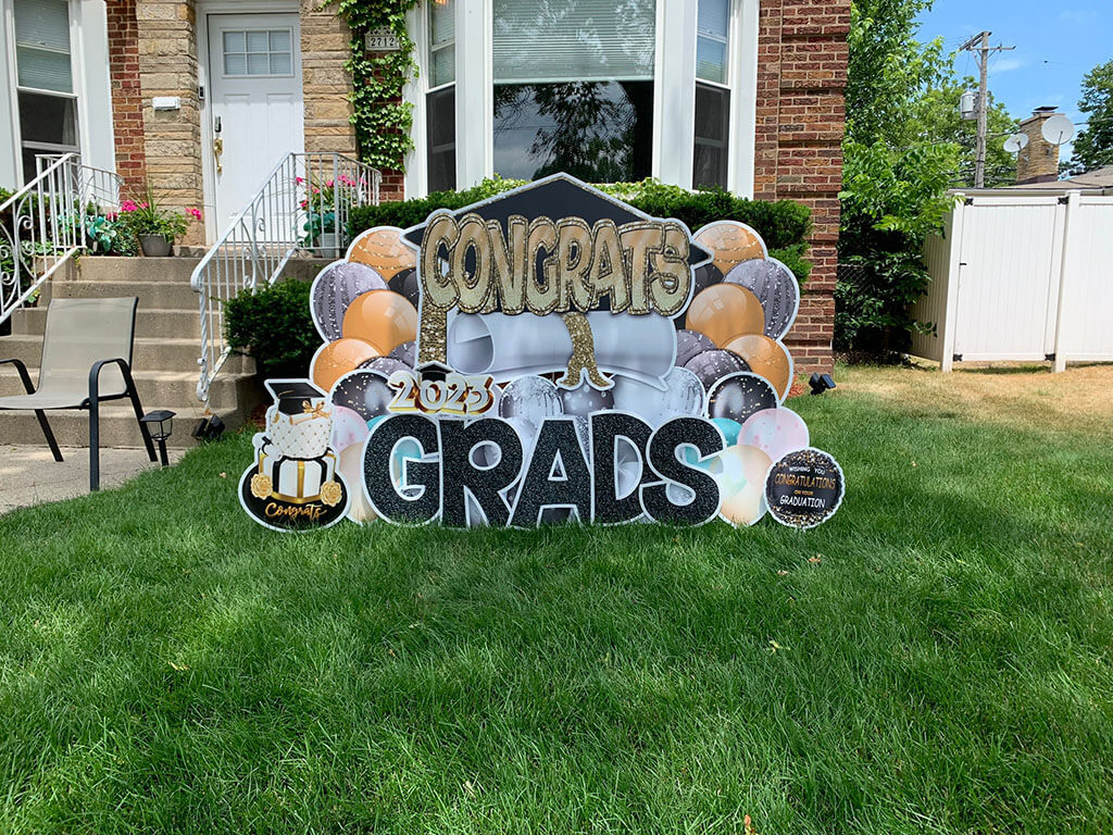 A photo of a custom made yard sign which reads Congrats Grads